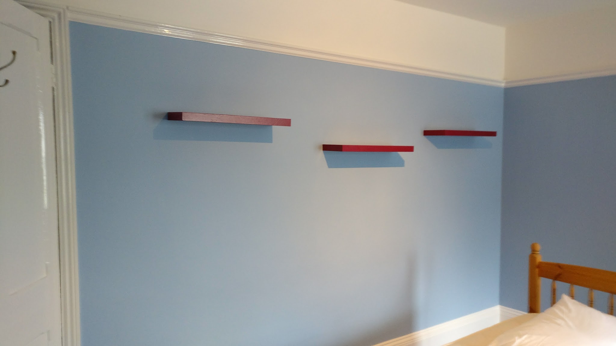 Pale blue bedroom walls with three red floating shelves and glossed white woodwork