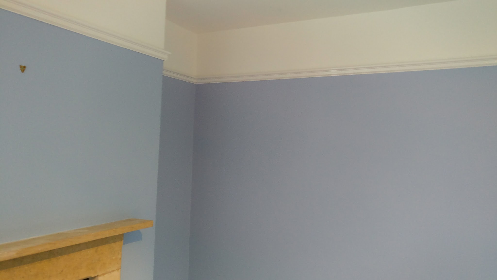 Corner of a redecorated room with blue walls, a white picture rail and a stone fireplace mantel